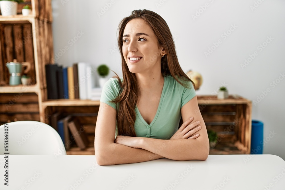 Young hispanic woman smiling confident sitting on table with arms crossed gesture at home Young hispanic woman smiling confident sitting on table with arms crossed gesture at home