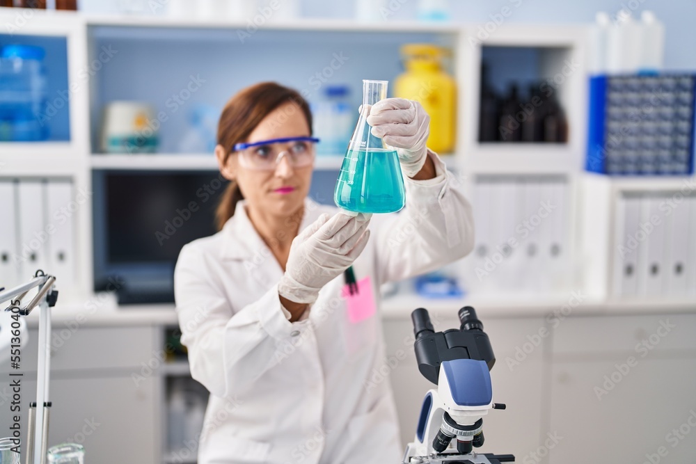 Fototapeta premium Middle age woman wearing scientist uniform measuring liquid at laboratory