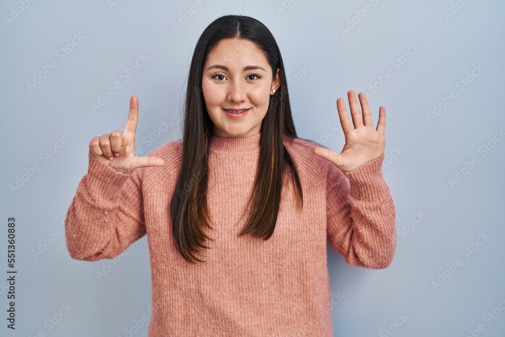 Young latin woman standing over blue background showing and pointing up with fingers number seven while smiling confident and happy. Young latin woman standing over blue background showing and pointing up with fingers number seven while smiling confident and happy.