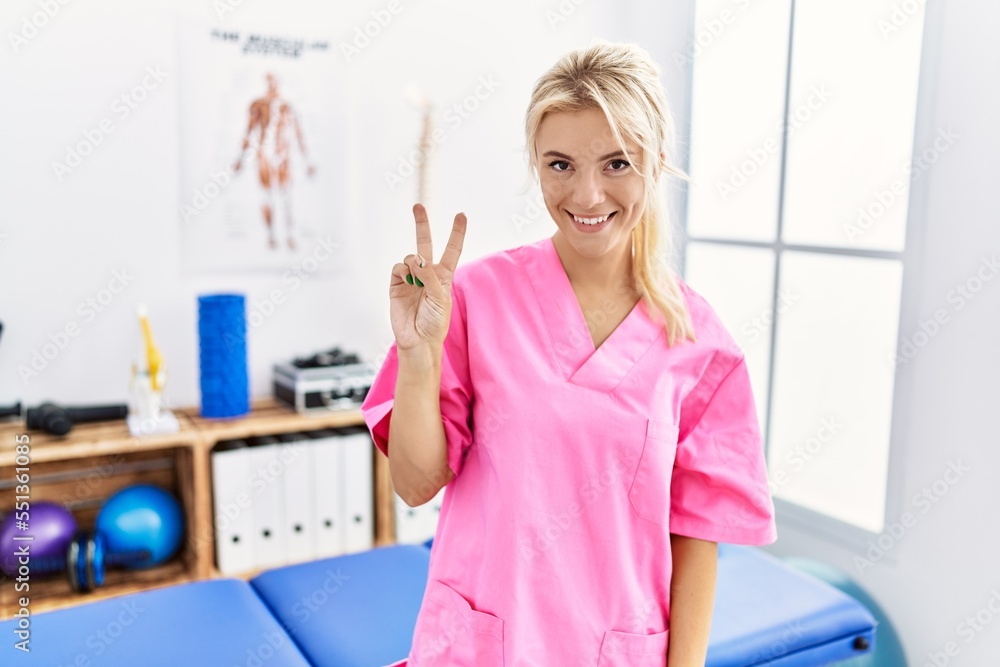 Young caucasian woman working at pain recovery clinic showing and pointing up with fingers number two while smiling confident and happy. Young caucasian woman working at pain recovery clinic showing and pointing up with fingers number two while smiling confident and happy.