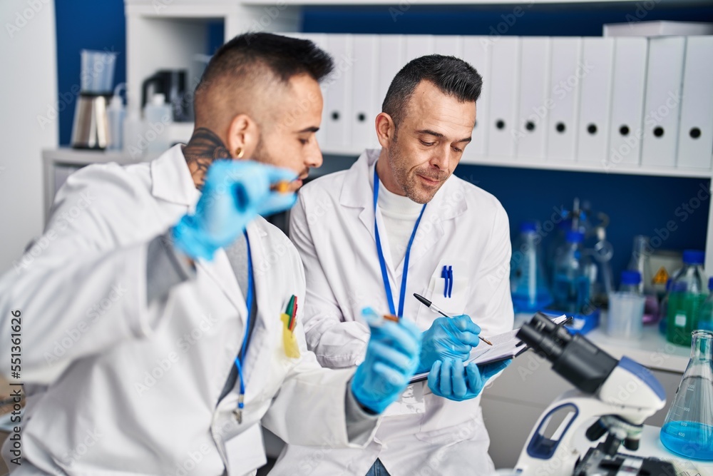 Two men scientist writing on document holding pills at laboratory Two men scientist writing on document holding pills at laboratory