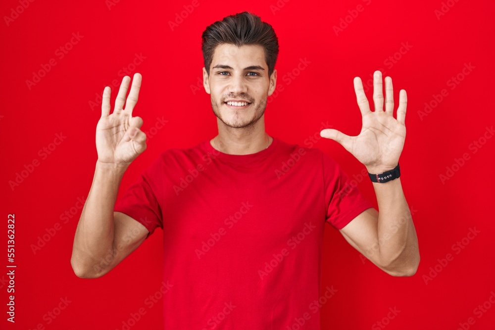 Young hispanic man standing over red background showing and pointing up with fingers number eight while smiling confident and happy.