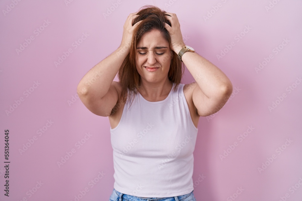 Brunette woman standing over pink background suffering from headache desperate and stressed because pain and migraine. hands on head. Brunette woman standing over pink background suffering from headache desperate and stressed because pain and migraine. hands on head.