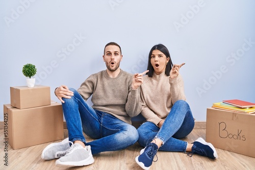 Young couple moving to a new home surprised pointing with finger to the side, open mouth amazed expression. © Krakenimages.com