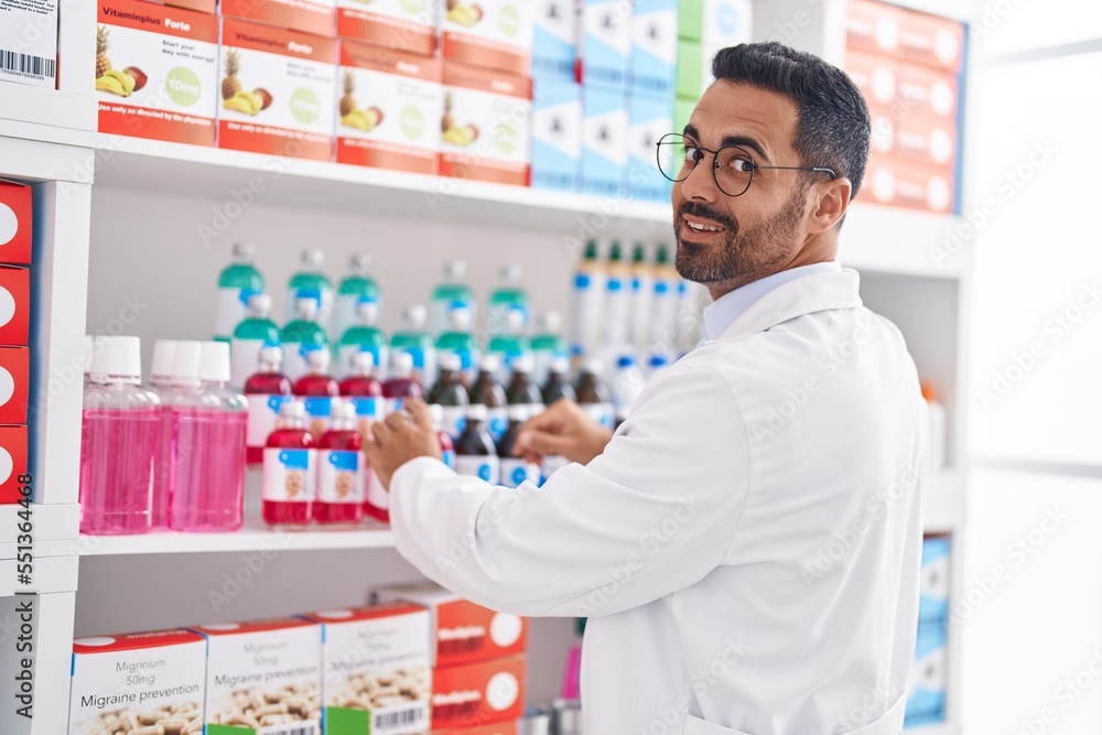 Young hispanic man pharmacist organizing shelving at pharmacy