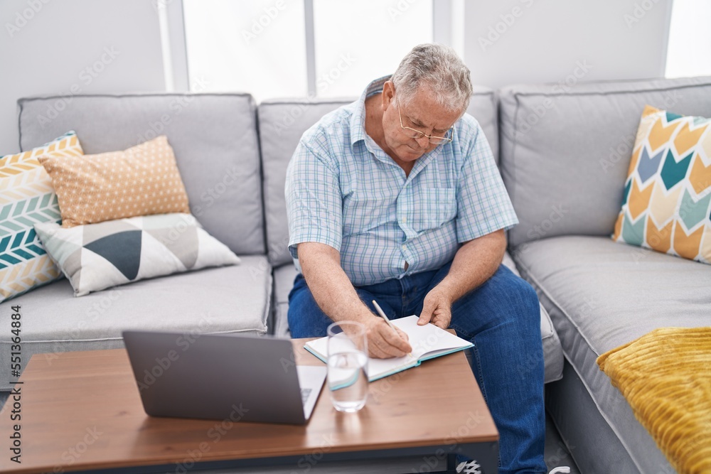 Middle age grey-haired man using laptop writing on notebook at home Middle age grey-haired man using laptop writing on notebook at home