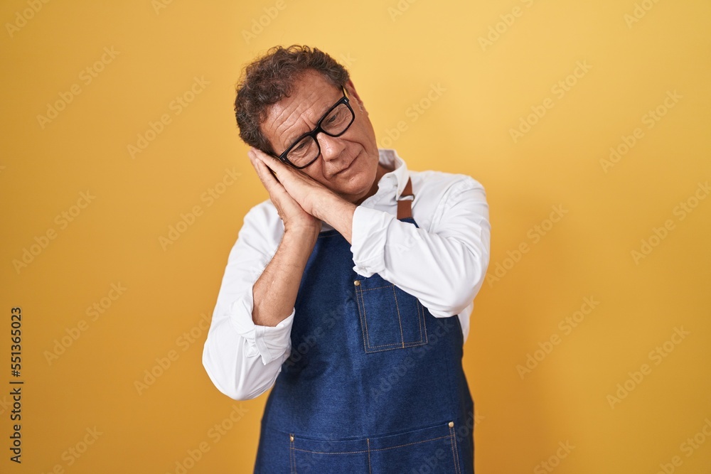 Middle age hispanic man wearing professional cook apron sleeping tired dreaming and posing with hands together while smiling with closed eyes. Middle age hispanic man wearing professional cook apron sleeping tired dreaming and posing with hands together while smiling with closed eyes.