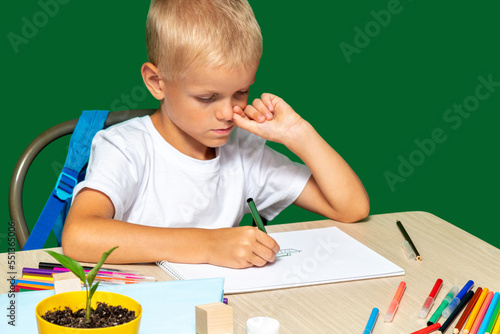 Focused boy draws with felt-tip pen on paper. On table there are pencils, brush, book, cubes, paints. Free time, learning to draw, hobbies. Selective focus.