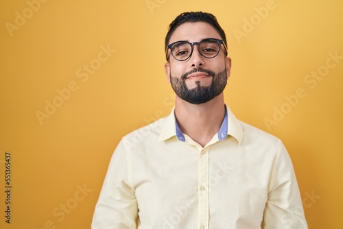 Hispanic young man wearing business clothes and glasses with hands together and crossed fingers smiling relaxed and cheerful. success and optimistic