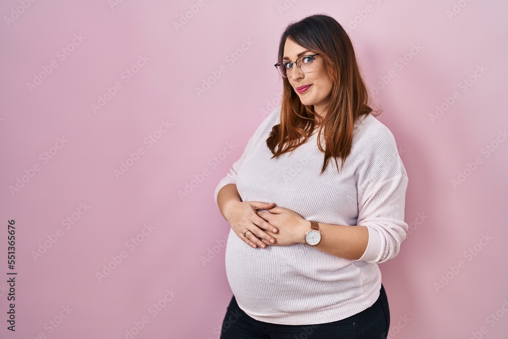Pregnant woman standing over pink background smiling looking to the side and staring away thinking. Pregnant woman standing over pink background smiling looking to the side and staring away thinking.
