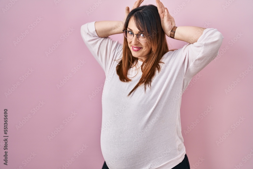 Pregnant woman standing over pink background doing bunny ears gesture with hands palms looking cynical and skeptical. easter rabbit concept. Pregnant woman standing over pink background doing bunny ears gesture with hands palms looking cynical and skeptical. easter rabbit concept.