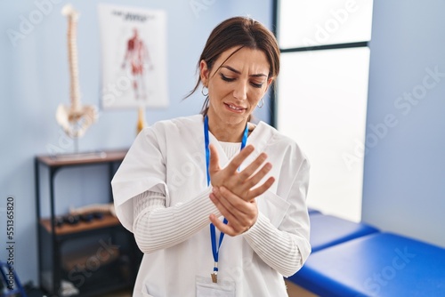 Young brunette woman working at pain recovery clinic suffering pain on hands and fingers  arthritis inflammation