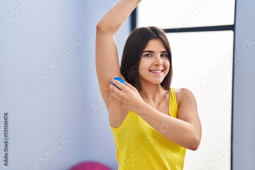 Young beautiful hispanic woman applying deodorant at sport center
