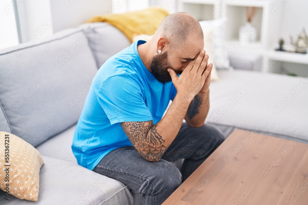 Young bald man stressed sitting on sofa at home