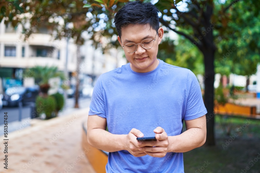 Obraz premium Young chinese man smiling confident using smartphone at park