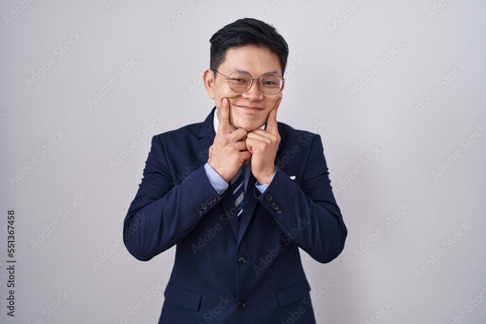 Young asian man wearing business suit and tie smiling with open mouth, fingers pointing and forcing cheerful smile Young asian man wearing business suit and tie smiling with open mouth, fingers pointing and forcing cheerful smile