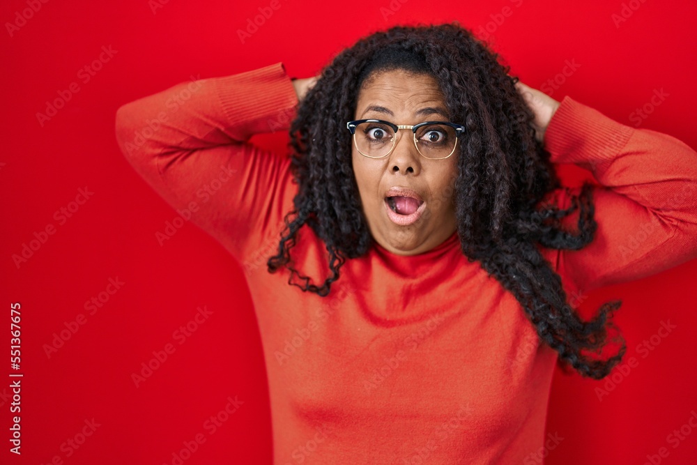 Plus size hispanic woman standing over red background crazy and scared with hands on head, afraid and surprised of shock with open mouth Plus size hispanic woman standing over red background crazy and scared with hands on head, afraid and surprised of shock with open mouth