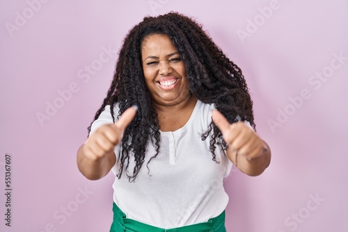Plus size hispanic woman standing over pink background approving doing positive gesture with hand, thumbs up smiling and happy for success. winner gesture.