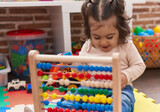 Adorable hispanic girl playing with abacus sitting on floor at kindergarten
