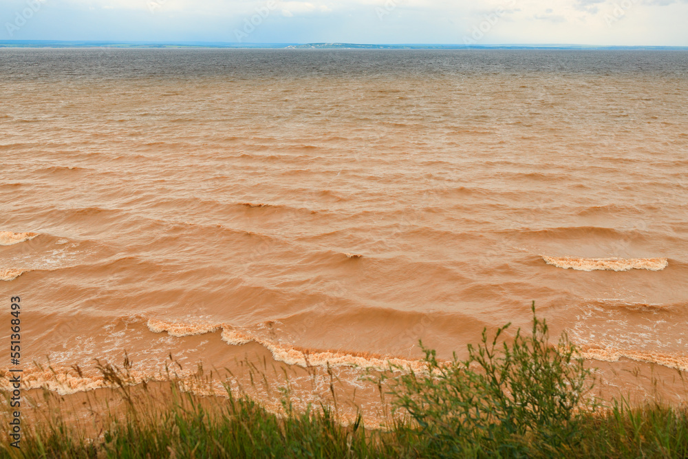 natural landscape of a large river with yellow dirty water and part of the bank on which grass grows natural landscape of a large river with yellow dirty water and part of the bank on which grass grows