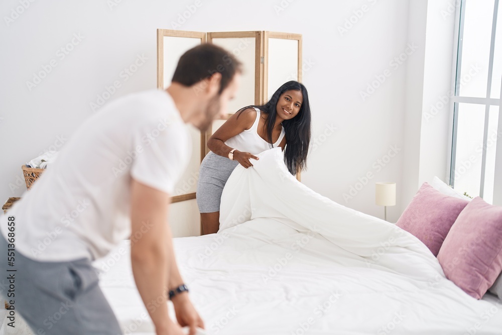 Man and woman interracial couple making bed at bedroom Man and woman interracial couple making bed at bedroom