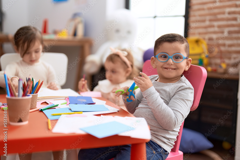 Fototapeta premium Adorable girl and boy sitting on table cutting paper at kindergarten