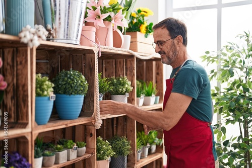 Middle age man florist holding plant of shelving at florist photo