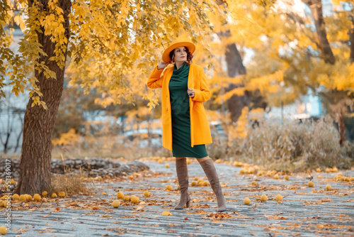 Beautiful woman walks outdoors in autumn. She is wearing a yellow coat, yellow hat and green dress. Young woman enjoying the autumn weather. Autumn content