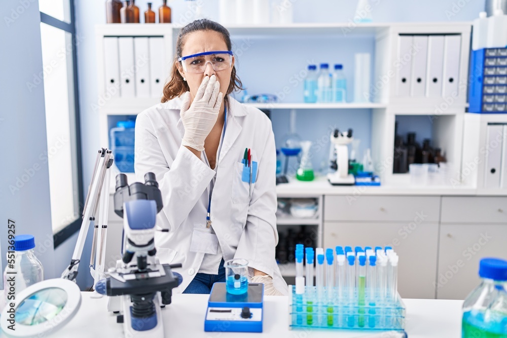 Young hispanic woman working at scientist laboratory bored yawning tired covering mouth with hand. restless and sleepiness. Young hispanic woman working at scientist laboratory bored yawning tired covering mouth with hand. restless and sleepiness.