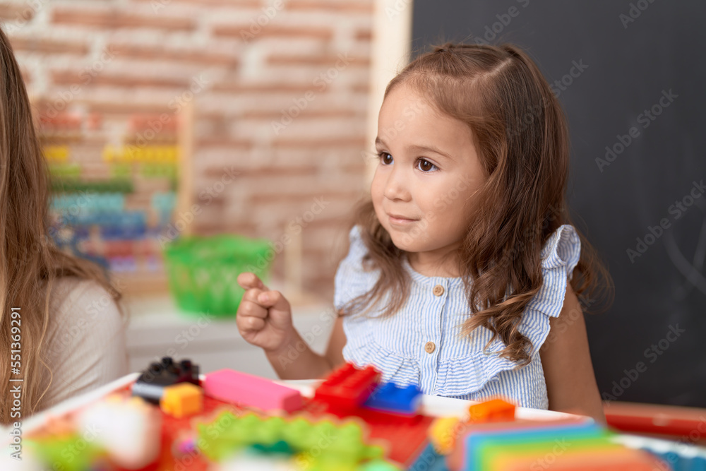 Fototapeta premium Adorable hispanic girl playing with construction blocks sitting on table at kindergarten