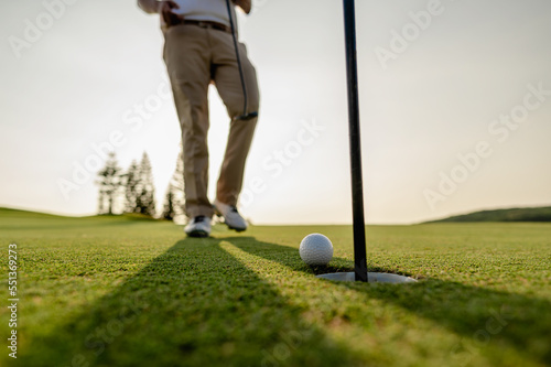 Golfer putting golf ball on golf course,he is walking to collect golf balls,lens flare on evening sun.Professional golf course at sunset. Summer,copy space,golf,nature,sport and weekend activities.