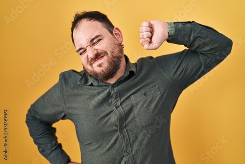 Plus size hispanic man with beard standing over yellow background stretching back, tired and relaxed, sleepy and yawning for early morning © Krakenimages.com