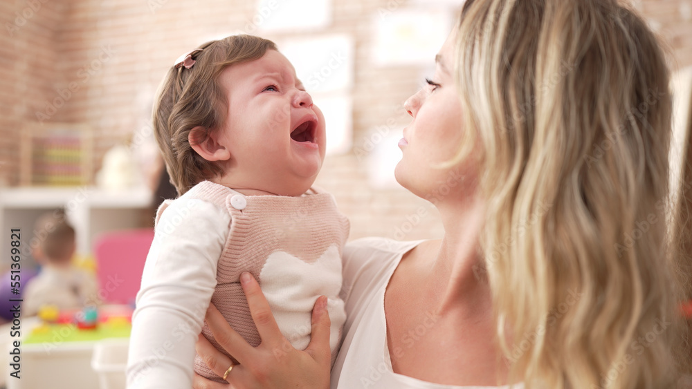 Mother and daughter consueling baby crying at kindergarten Mother and daughter consueling baby crying at kindergarten