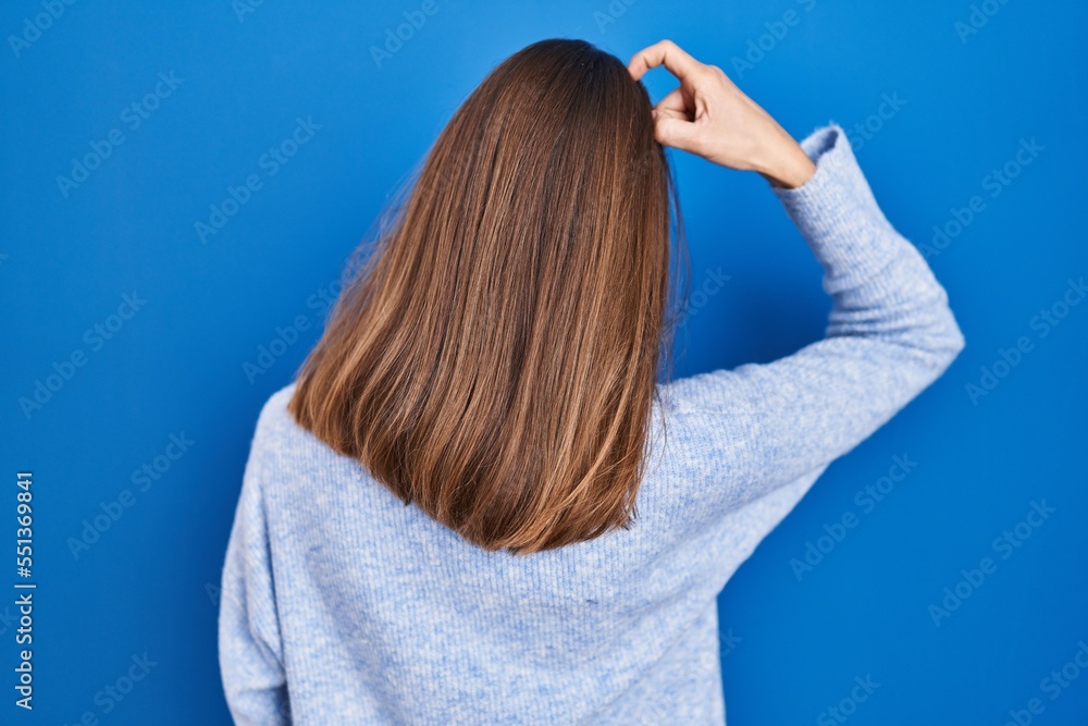 Fototapeta premium Young woman standing over blue background backwards thinking about doubt with hand on head