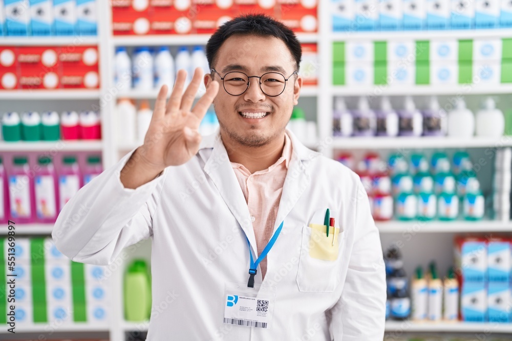 Chinese young man working at pharmacy drugstore showing and pointing up with fingers number four while smiling confident and happy. Chinese young man working at pharmacy drugstore showing and pointing up with fingers number four while smiling confident and happy.