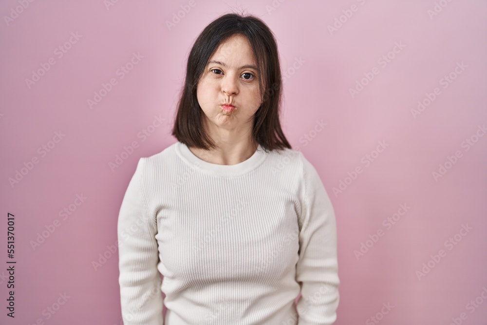 Woman with down syndrome standing over pink background puffing cheeks with funny face. mouth inflated with air, crazy expression. Woman with down syndrome standing over pink background puffing cheeks with funny face. mouth inflated with air, crazy expression.