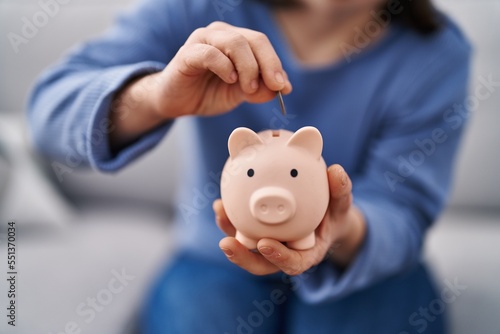 Young woman with down syndrome inserting coin on piggy bank at home