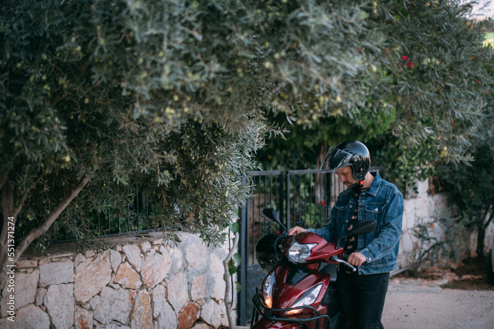 Naklejka premium A young man in a helmet starts a motorcycle near the gate of the house.