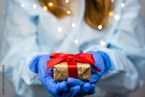 Doctor or nurse hands in medical gloves holds a gift box. Close-up. Selective focus.