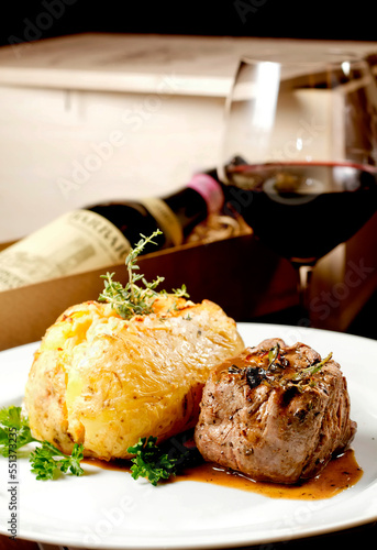 Filet mignon beef steak with gravy and stuffed potato served on a plate paired with red wine glass and bottle on background. Premium quality restaurant. Gourmet food. Mediterranean style cuisine meal.