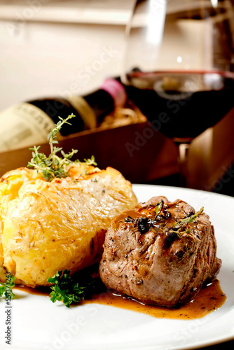 Filet mignon beef steak with gravy and stuffed potato served on a plate paired with red wine glass and bottle on background. Premium quality restaurant. Gourmet food. Mediterranean style cuisine meal.