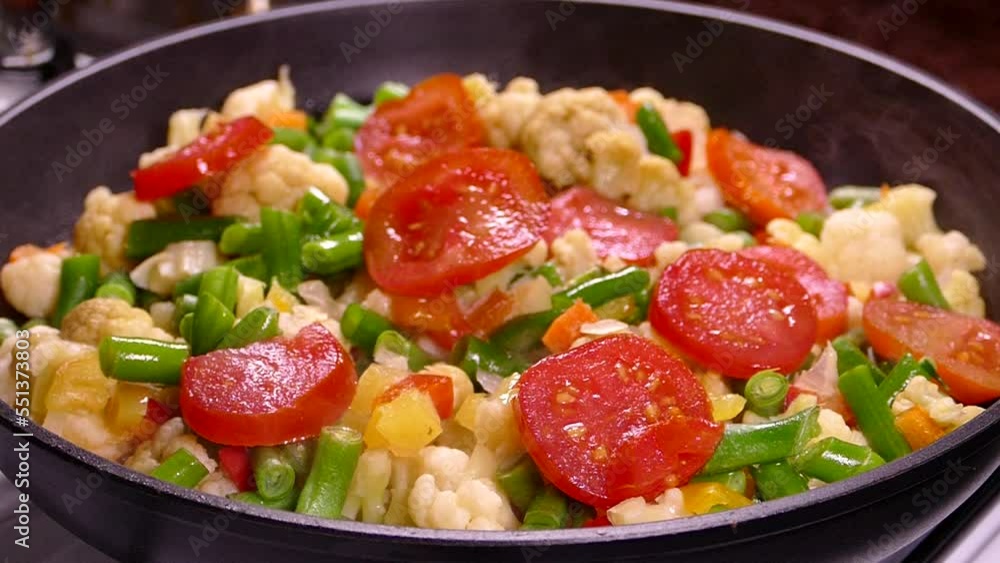 Cooking vegetable stew from frozen chopped vegetables. Tomatoes, asparagus and cabbage are steaming in a pan. Cooking vegetable stew from frozen chopped vegetables. Tomatoes, asparagus and cabbage are steaming in a pan.