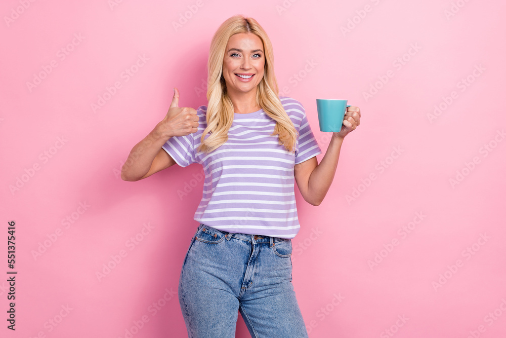 Photo of smiling blonde hair business lady wear trendy t-shirt thumb up like symbol hold cup morning coffee isolated on pink color background Photo of smiling blonde hair business lady wear trendy t-shirt thumb up like symbol hold cup morning coffee isolated on pink color background