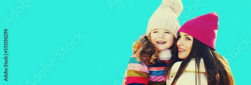 Winter portrait of happy smiling mother and little girl child looking away on blue background