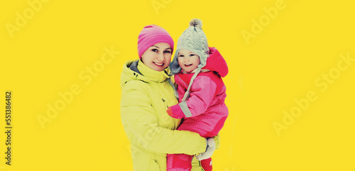 Winter portrait of happy smiling young mother and child on yellow background