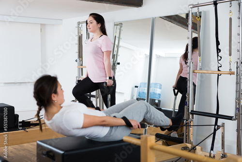 Positive young Latina practicing pilates stretching exercises on reformer at gym..