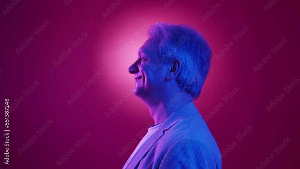 Neon light aged man. Profile portrait. Stylish look. Smiling elder male in suit posing on blue purple background halo headlight. Neon light aged man. Profile portrait. Stylish look. Smiling elder male in suit posing on blue purple background halo headlight.