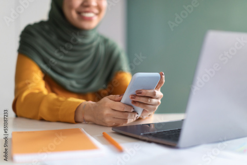 Muslim Woman In Hijab Using Mobile Phone While Sitting At Desk In Office