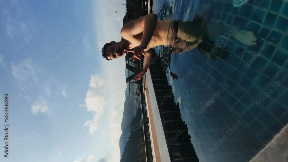 Caucasian bearded man is resting in open swimming pool and enjoying mountain view from it. Vertical footage of male blogger resting on villa in Thailand and shooting content talking to his followers Caucasian bearded man is resting in open swimming pool and enjoying mountain view from it. Vertical footage of male blogger resting on villa in Thailand and shooting content talking to his followers