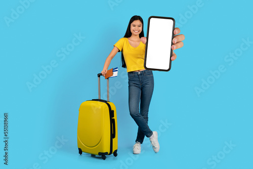 Cheerful pretty millennial korean woman student blogger with suitcase, tickets show smartphone with blank screen